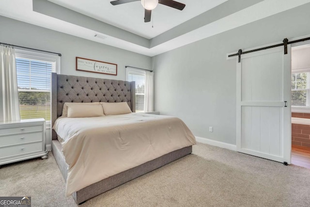 bedroom featuring a barn door, light carpet, ceiling fan, and a tray ceiling