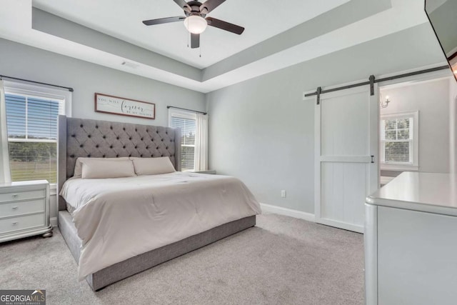 carpeted bedroom featuring multiple windows, a raised ceiling, ceiling fan, and a barn door