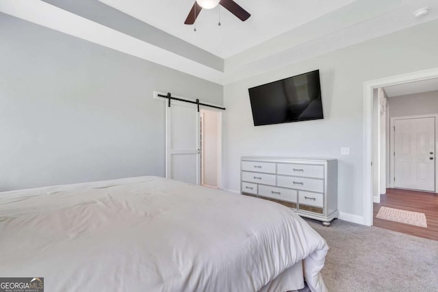 carpeted bedroom with a barn door and ceiling fan