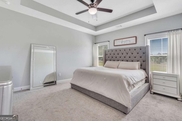 bedroom featuring a raised ceiling, light carpet, and ceiling fan