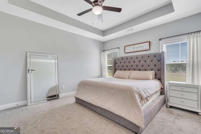 carpeted bedroom featuring multiple windows, ceiling fan, and a tray ceiling