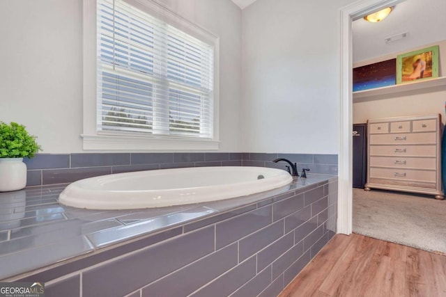 bathroom with hardwood / wood-style flooring and tiled tub