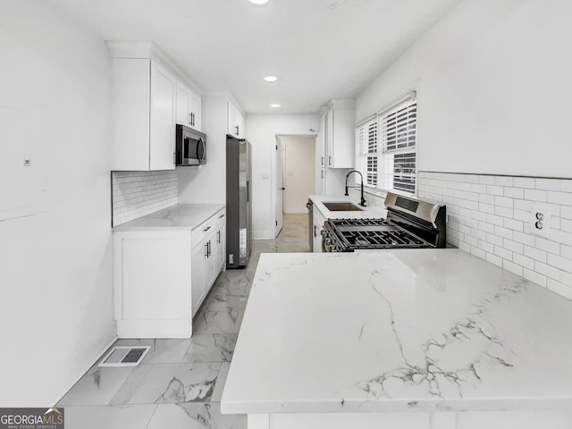 kitchen with stainless steel appliances, sink, white cabinets, and light stone counters