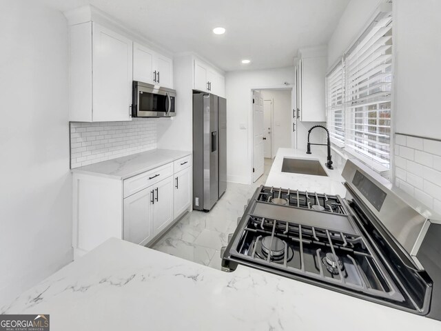 kitchen with sink, tasteful backsplash, stainless steel appliances, light stone countertops, and white cabinets