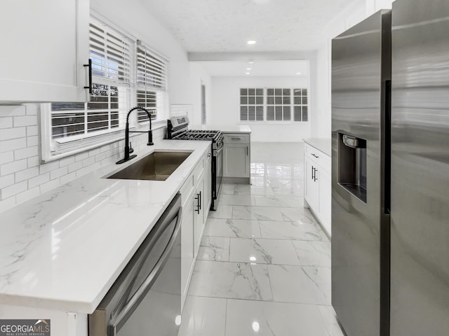 kitchen featuring appliances with stainless steel finishes, sink, white cabinets, light stone counters, and a textured ceiling