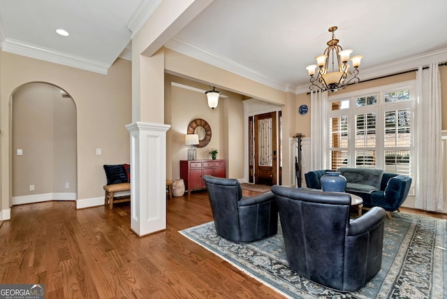 living room featuring an inviting chandelier, crown molding, dark wood-type flooring, and decorative columns