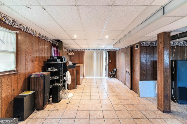 basement with a paneled ceiling, light tile patterned floors, and wood walls