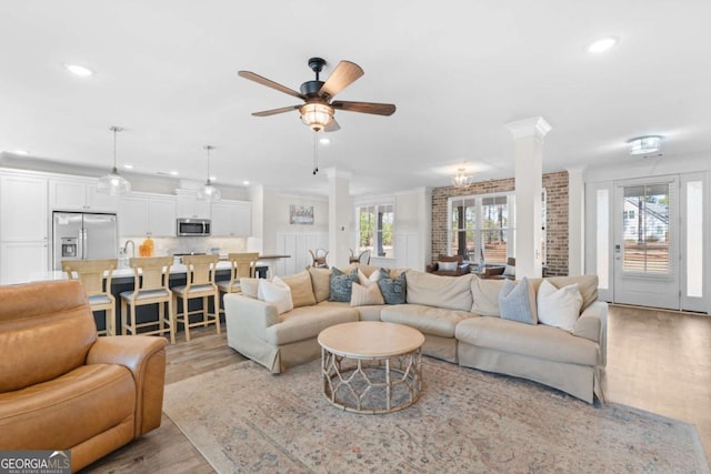 living room featuring ornate columns, ceiling fan, crown molding, and light wood-type flooring