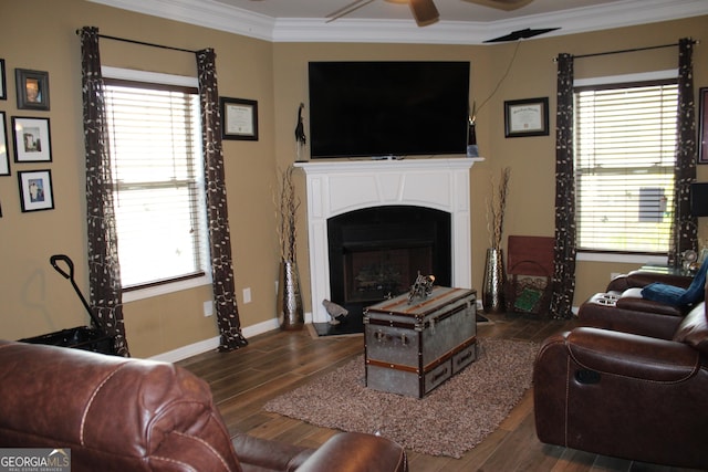 living area featuring dark wood-type flooring, a ceiling fan, baseboards, ornamental molding, and a glass covered fireplace