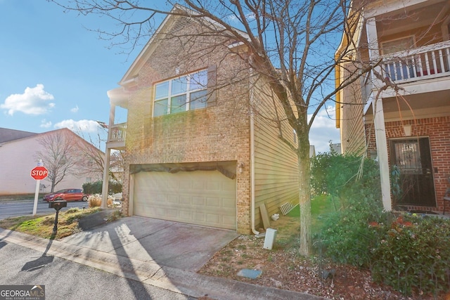 view of side of home featuring concrete driveway, brick siding, a balcony, and an attached garage