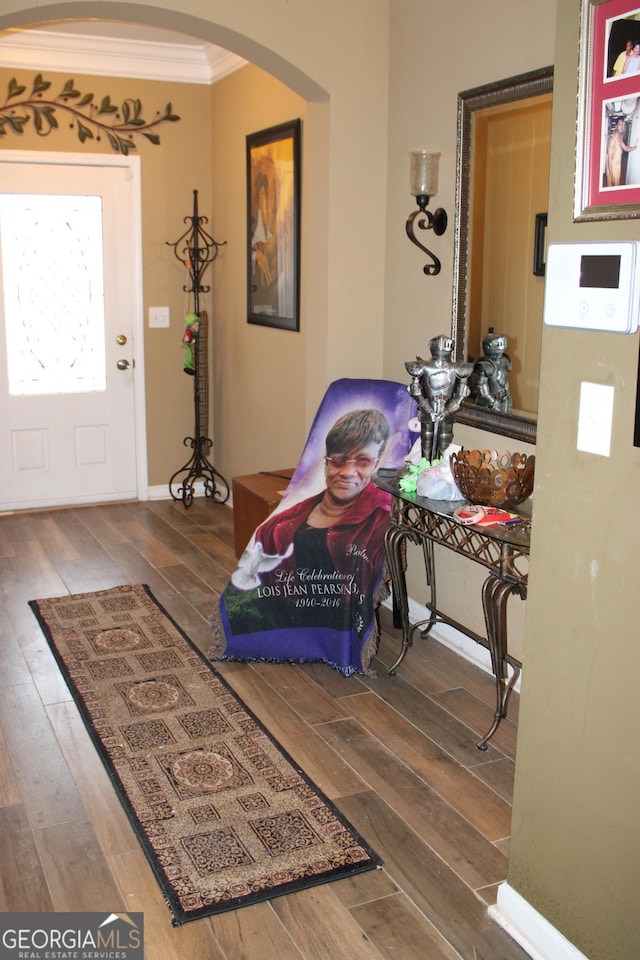 foyer entrance featuring arched walkways, ornamental molding, and wood finished floors