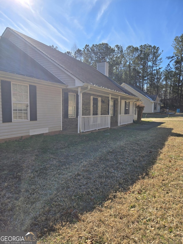 back of house featuring covered porch, a chimney, and a lawn