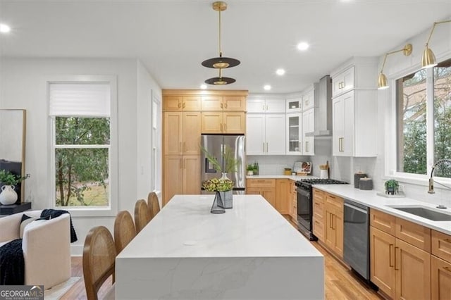 kitchen featuring tasteful backsplash, wall chimney exhaust hood, stainless steel appliances, light countertops, and a sink