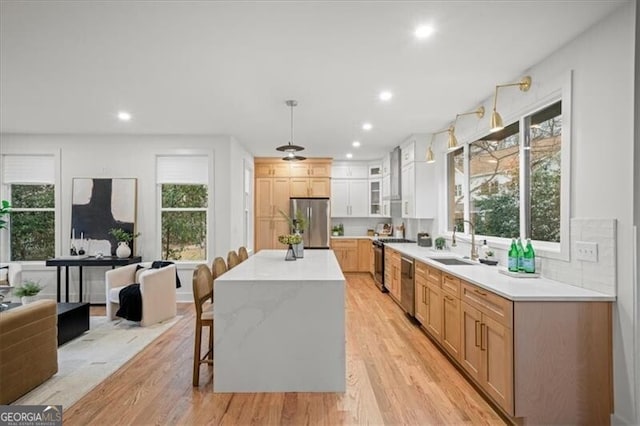 kitchen with light wood-style flooring, stainless steel appliances, a sink, light countertops, and a center island