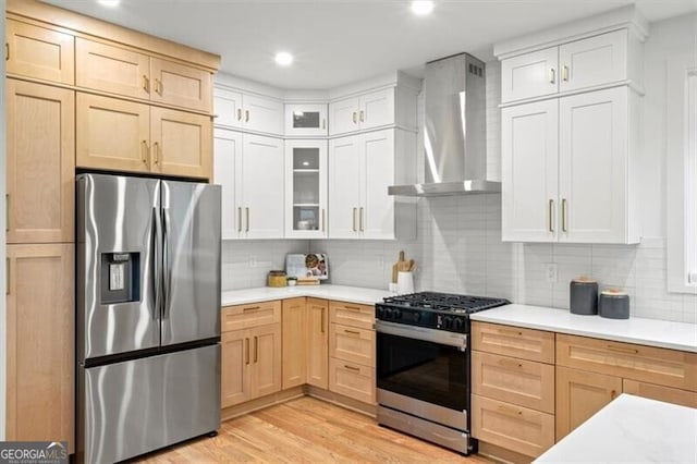 kitchen featuring wall chimney exhaust hood, stainless steel appliances, light countertops, and light brown cabinetry