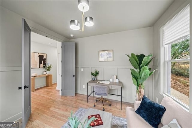 office area with a chandelier, light wood-type flooring, wainscoting, and a decorative wall