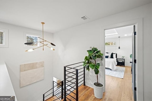 corridor featuring visible vents, a chandelier, wood finished floors, and an upstairs landing