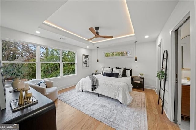 bedroom with light wood-type flooring, baseboards, and a tray ceiling