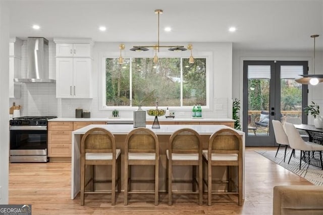 kitchen with a kitchen island, light countertops, stainless steel gas range, decorative backsplash, and wall chimney exhaust hood