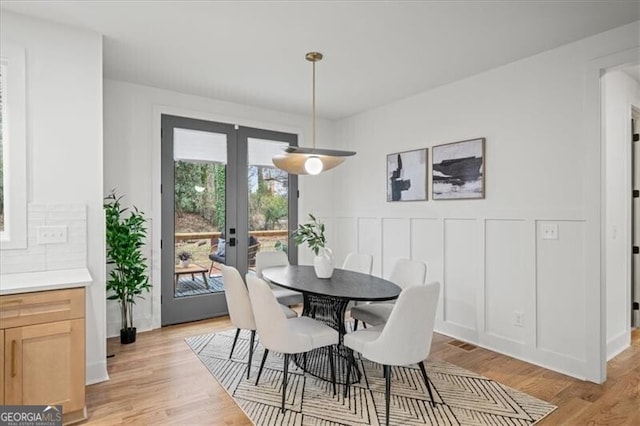 dining area featuring visible vents, french doors, light wood-style flooring, and a decorative wall