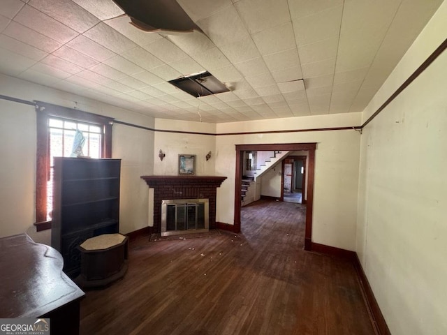 unfurnished living room with a brick fireplace and dark wood-type flooring