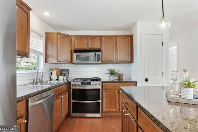 kitchen with stone countertops, hanging light fixtures, light hardwood / wood-style flooring, stainless steel appliances, and decorative backsplash