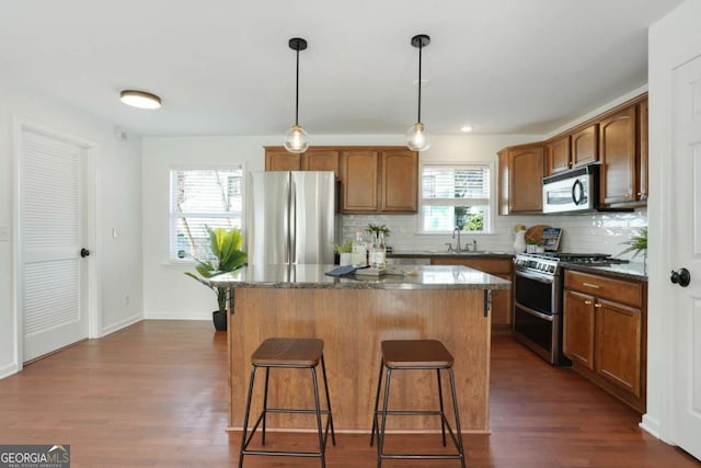 kitchen with sink, dark wood-type flooring, stainless steel appliances, a kitchen island, and decorative light fixtures