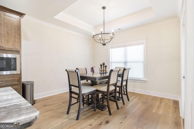 dining area featuring crown molding, baseboards, a raised ceiling, and light wood-style floors