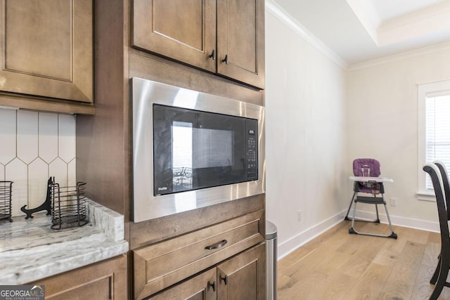 kitchen featuring baseboards, ornamental molding, light wood-type flooring, built in microwave, and a tray ceiling