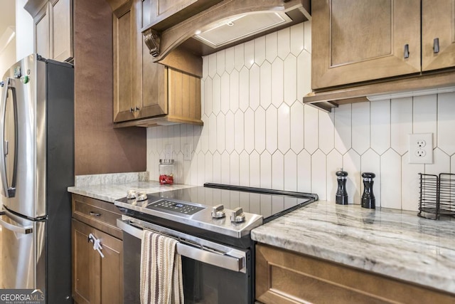 kitchen with custom range hood, light stone counters, stainless steel appliances, and backsplash