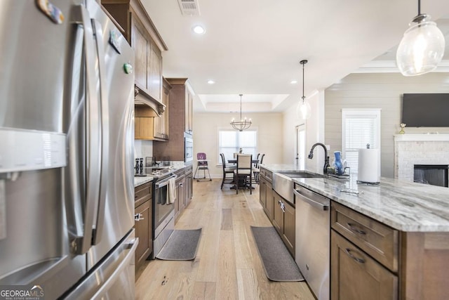 kitchen with a tray ceiling, recessed lighting, appliances with stainless steel finishes, light wood-style floors, and a sink