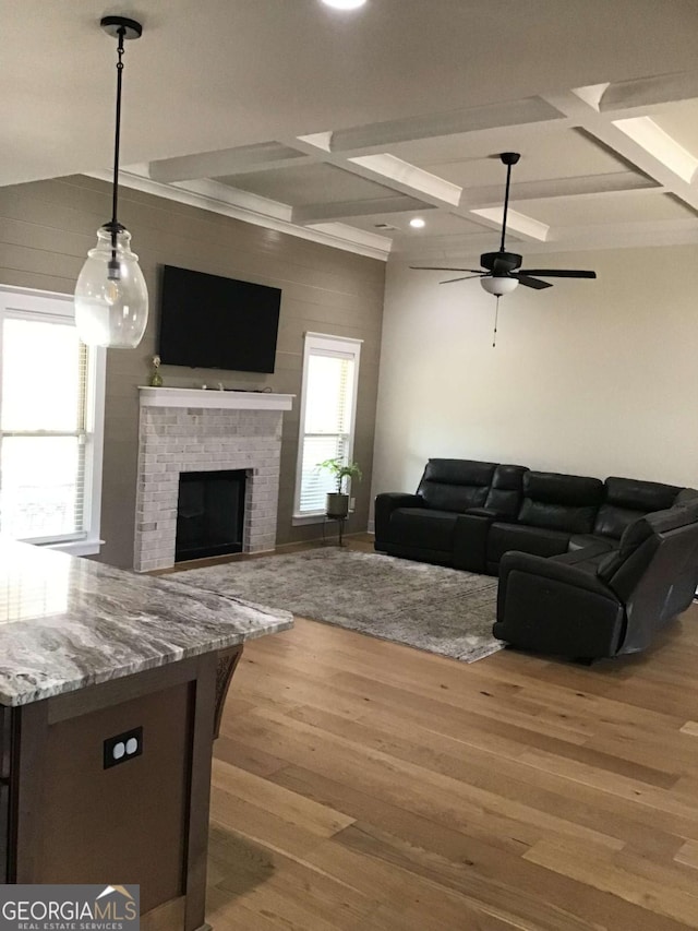 living room featuring ceiling fan, beam ceiling, coffered ceiling, a brick fireplace, and light wood-type flooring