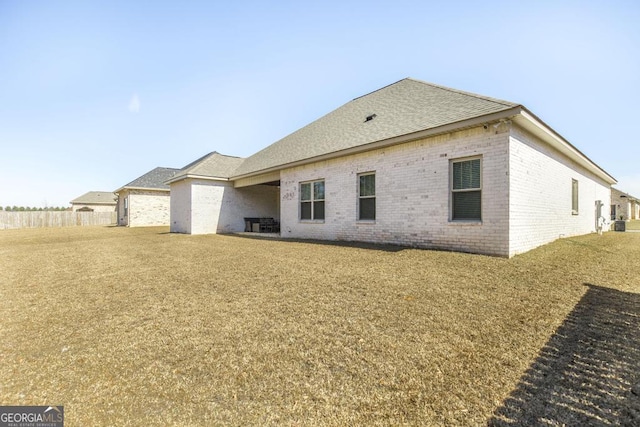 rear view of house featuring a yard, brick siding, and a shingled roof