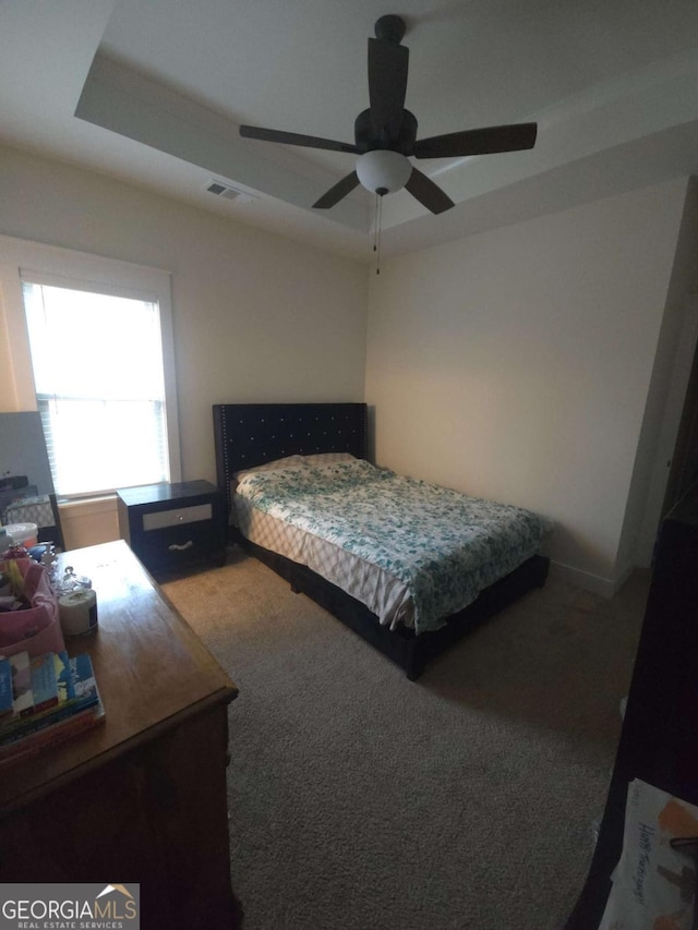 carpeted bedroom with ceiling fan and a tray ceiling