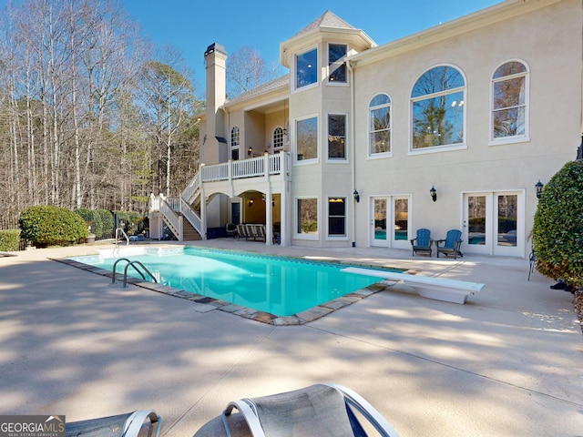 pool with a diving board, french doors, a patio, and stairs