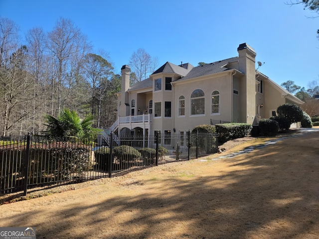 view of side of property with stairs, a chimney, fence private yard, and stucco siding