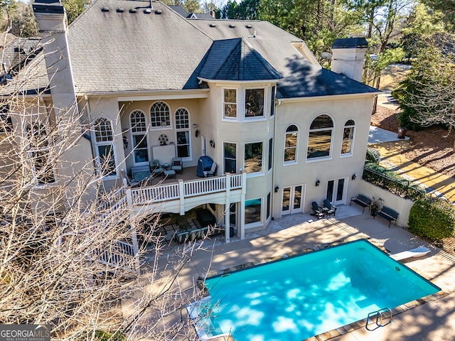 back of house featuring a fenced in pool, french doors, roof with shingles, a chimney, and stucco siding