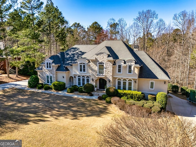 french provincial home with stone siding, a shingled roof, driveway, and stucco siding