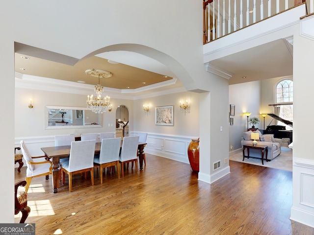 dining room featuring a tray ceiling, visible vents, ornamental molding, wainscoting, and wood finished floors