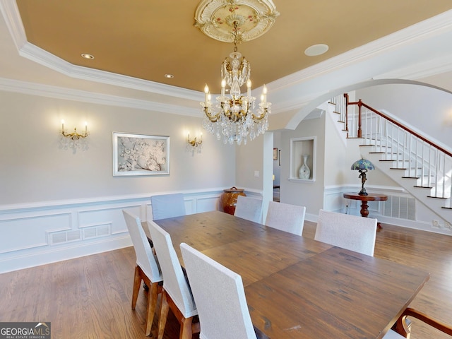 dining area featuring visible vents, arched walkways, stairway, wood finished floors, and a tray ceiling