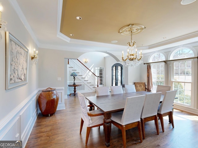 dining room featuring arched walkways, a decorative wall, wood finished floors, stairs, and a raised ceiling