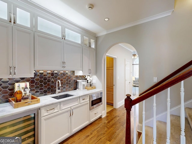 kitchen featuring wine cooler, arched walkways, stainless steel microwave, white cabinetry, and a sink