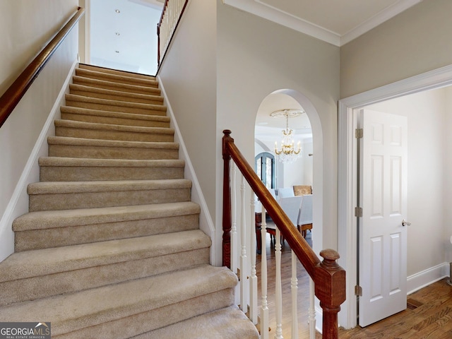 stairway featuring baseboards, ornamental molding, arched walkways, and wood finished floors