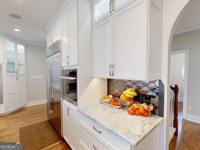 kitchen featuring arched walkways, white cabinets, stainless steel appliances, light wood-type flooring, and backsplash