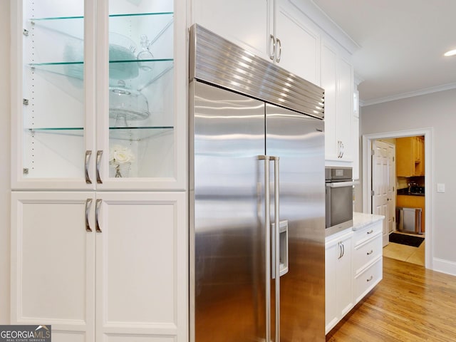 kitchen with stainless steel appliances, white cabinets, ornamental molding, and light wood finished floors