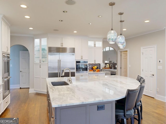 kitchen featuring arched walkways, stainless steel appliances, crown molding, a large island with sink, and a sink