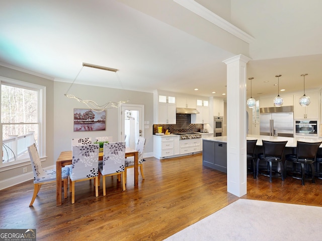 dining area with baseboards, dark wood-style flooring, decorative columns, and crown molding