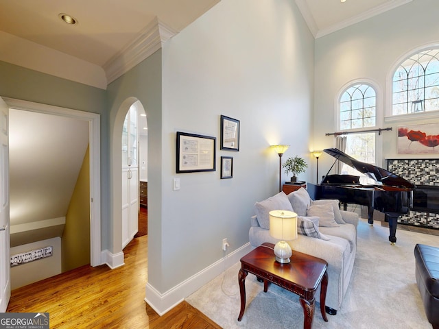 sitting room featuring arched walkways, crown molding, baseboards, and wood finished floors