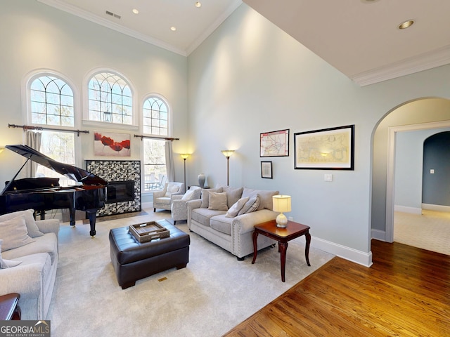 living area with visible vents, arched walkways, a tile fireplace, a towering ceiling, and ornamental molding