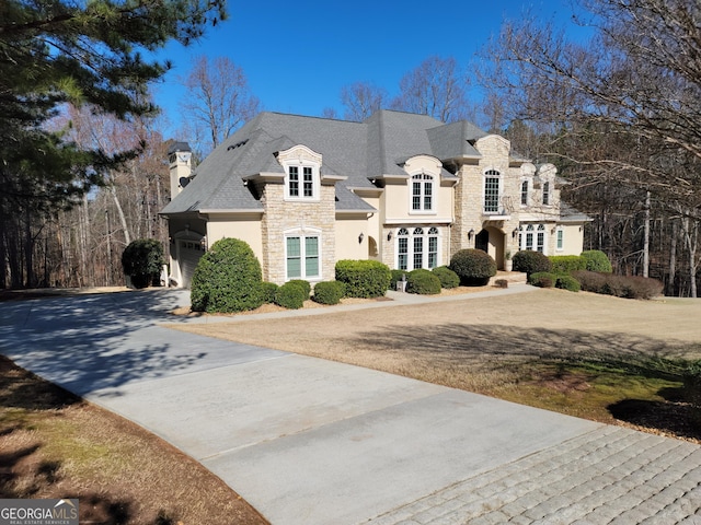 french provincial home with an attached garage, stone siding, a chimney, and concrete driveway